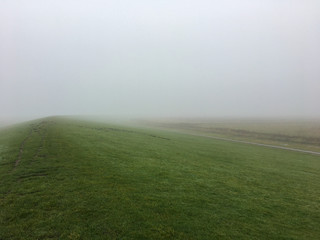 Obraz premium A Dyke in the Mist on a foggy day in East Frisia, in the North of Germany near Pilsum. Northsea coast