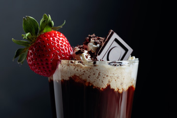 Coffee cocktail with whipped cream, strawberry and pieces of black chocolate .