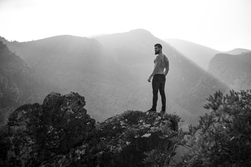 Man on a rock at the mountains with the sun behind