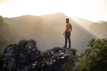 Man on a rock at the mountains with the sun behind