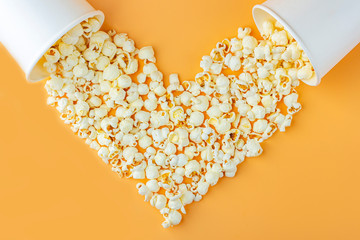 Love movies concept. Popcorn in paper box scattered on orange background heart shaped top view, copy space for text. Cinema snack concept. Popcorn box mocap