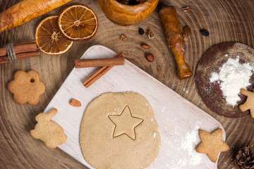 Christmas homemade baking background: ginger dough rolled out on a wooden board, cookies, cinnamon and slices of dried oranges. Top view, flat lay, copy space.