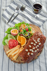 Delicious barbecued ribs seasoned with a spicy basting sauce and served with chopped fresh herbs and salad on an old rustic wooden chopping board.