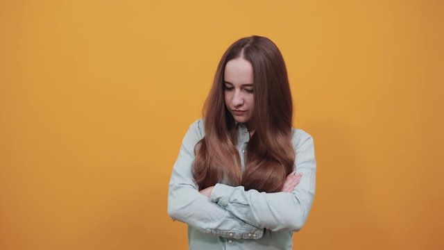 Serious caucasian brunette woman in denim blue shirt crossed hands, looking agressive isolated on orange background in studio. People emotions, lifestyle concept.
