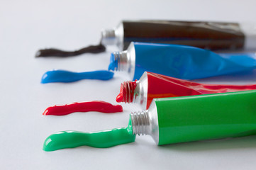 Close up of paint tubes with green and red blue and black color lying in a row. Color stripes coming out of the tubes. Colorful image from an artist&rsquo;s studio or a school showing creative education. 
