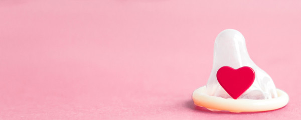 open condom and a red little heart on a pink background, place for text