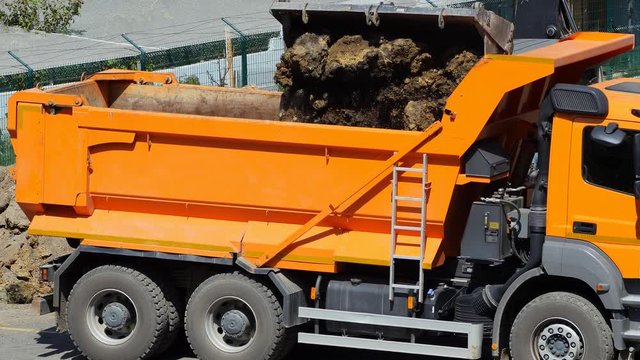Excavator loading soil on a dump truck. Crawler dozer and tipper working at the construction site