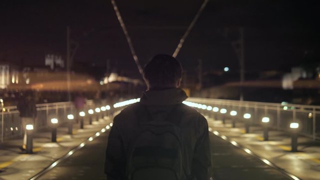 Back view cinematic of lonely man, walking down empty street, homeless abandoned hooded troubled guy wandering big city at night