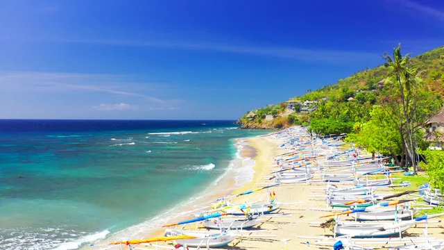 Drone moving forward over the white fisherman boats on the sand at Amed beach, surrounded by majestic green palms tree in Bali, Indonesia. Aerial view 4K