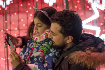 Father and daughter in christmas tree illuminated posing for photo looking the lights