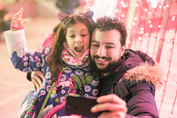 Father and daughter in christmas tree illuminated posing for photo looking the lights