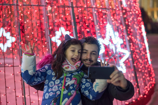 Father and daughter in christmas tree illuminated posing for photo looking the lights