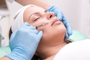 Obraz na płótnie Canvas injection into the skin of the face of a young woman, close-up. A cosmetologist with a syringe with a needle introduces a means to remove wrinkles on the face in the lip area.