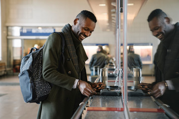 Happy stylish man buying ticket in train station