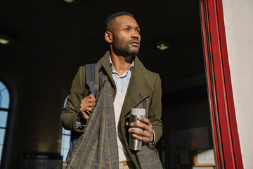 Stylish man with reusable cup getting out of the train station