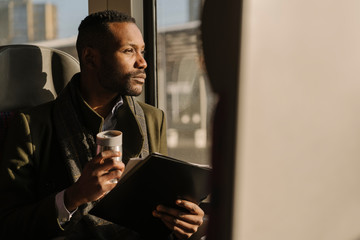 Portrait of stylish businessman with reusable cup and documents inside a train