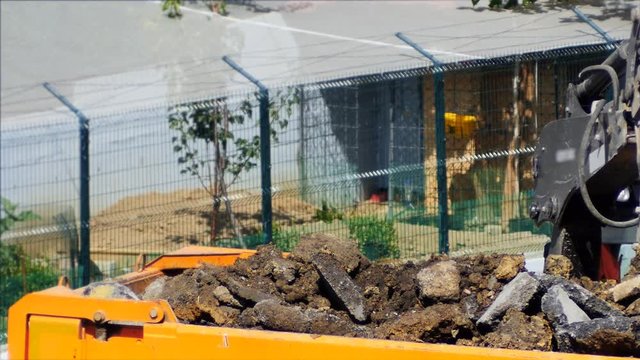 Backhoe loader levels and compacts garbage in a dump truck. Dump truck being loaded with soil by an excavator. Close up, original HD video. Construction machinery working at the construction site