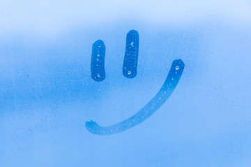 The picture or figure of the smiling face on the blue evening or morning window glass with drops 