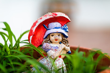 Weathered miniature garden figure of young girl with red umbrella