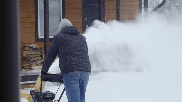 A man cleans snow with a snow blower near his house.