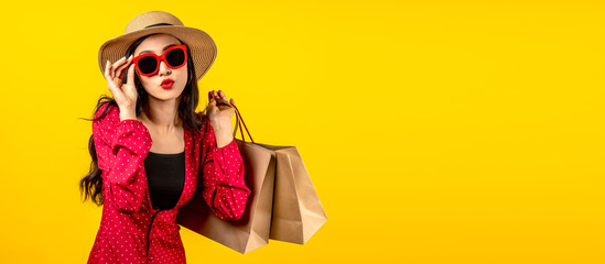 Banner of Asian trendy shopaholic woman excited about new purchases or sales holding shopping bags and looking to camera over yellow background. Happy Asian customer carrying shopping bags.