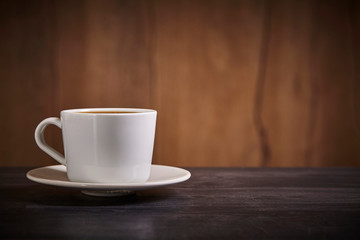 White cup of coffee on brown wooden background with copy space. Close up.