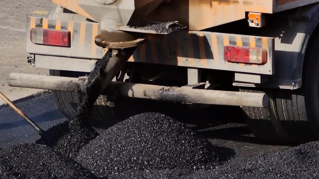 Truck dumping hot asphalt on the road. Large industrial machine pour asphaltic concrete on the street. The dump truck unloads rubble for laying roads. Hauling & dumping asphalt into paver site