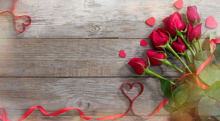 Fototapeta na wymiar Valentine greeting card background. Roses and red heart ribbon on old table