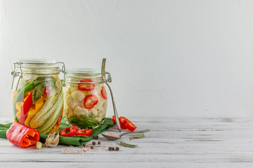 two glass jars of fermented cauliflower, cucumbers, onions, vegetables on a light background. using textile green. fermentation is a source of probiotic. popular vegetarian food. copy space