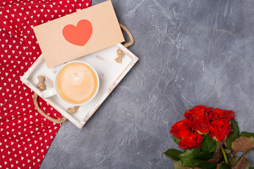 Valentine's Day concept. Morning coffee, envelope with red heart, roses on grey desk. Free space....