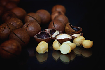 Peeled and unpeeled macadamia nuts on a black background