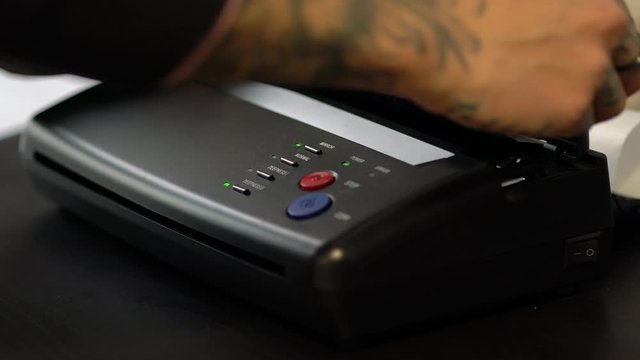 Tattoo artist printing stencil sketch on the pinter to make a new tattoo