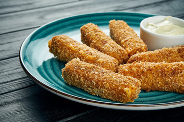 Delicious close up view on Deep-fried fish or cheese sticks fried with white sauce on a blue plate on a black background. Bar snack for beer.