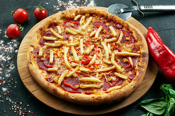 Delicious close up view on Spicy pizza with ham, French fries chili cheese. Traditional italian cuisine. Pizza in composition with ingridients on dark background