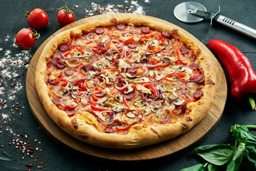 Pizza with a large number of toppings: hunting sausages, onions, mushrooms, salami, cheese and bell pepper. Pizza in composition with ingredients on a black background