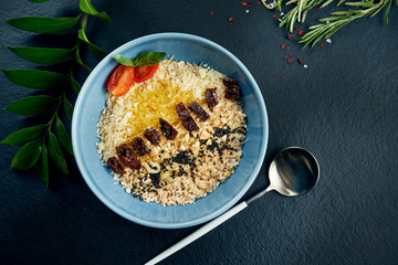 Healthy breakfast: oatmeal with sun-dried tomatoes, parmesan and butter in a blue bowl on a black background. Top view food flat lay. Copy space