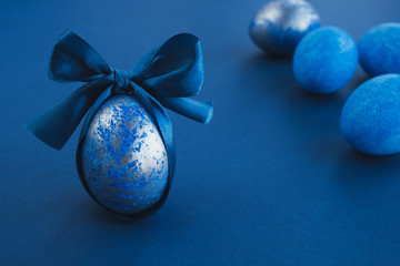 Blue easter egg with ribbon on dark background. Easter stylish minimal composition. Copy space, close up
