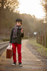 Adorable boy on a railway station, waiting for the train with suitcase