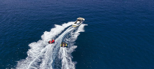 Aerial drone ultra wide photo of power boat towing children having fun with donut water-sports in deep blue Mediterranean bay