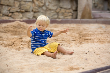 Little toddler boy, playing with sand in sandpit at the playground