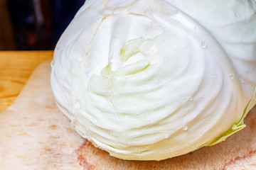Whole head of fresh white cabbage with water drops on the wooden cutting board