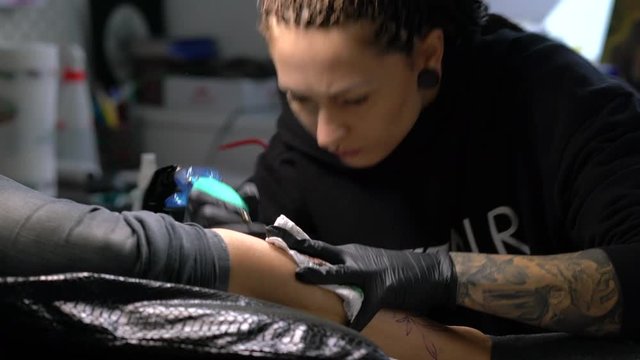 Tattoo female artist makes a tattoo on a female leg