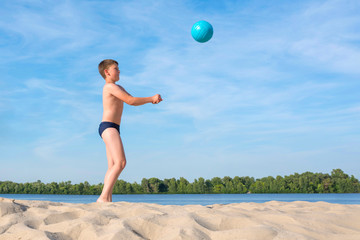  A boy plays beach volleyball.  Side view.  Sport lifestyle.