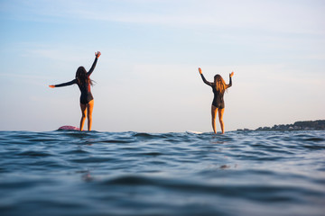 Water women friends surfing together at sunset