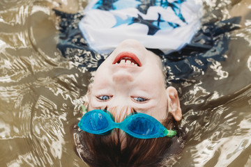 Boy wearing goggles floating in water looking at camera