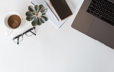 Top view of workspace with laptop, phone, glasses, notepad, coffee.