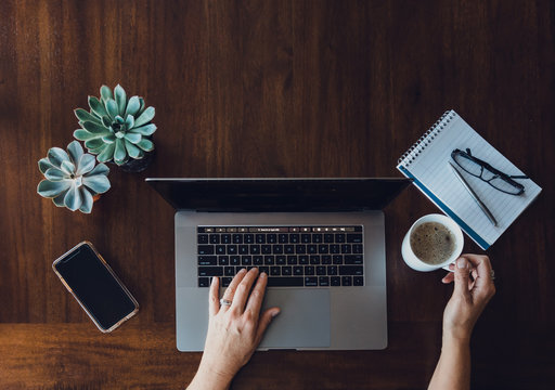 Overhead view of woman's hands working on laptop at wooden table.