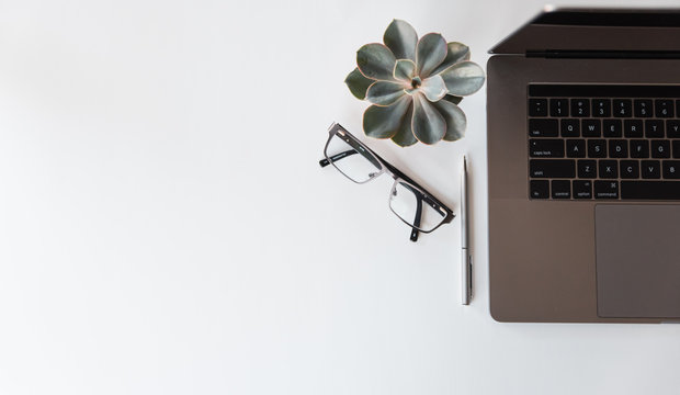 Overhead view of modern workspace with laptop, glasses and pen.