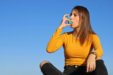 Young girl dressed in yellow taking the asthma inhaler.