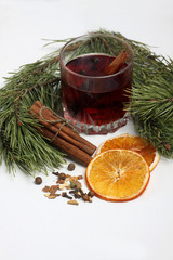 Obraz na płótnie Canvas glass of mulled wine, cinnamon sticks, spice and orange chips with fir bough on white background close up. Vertical image